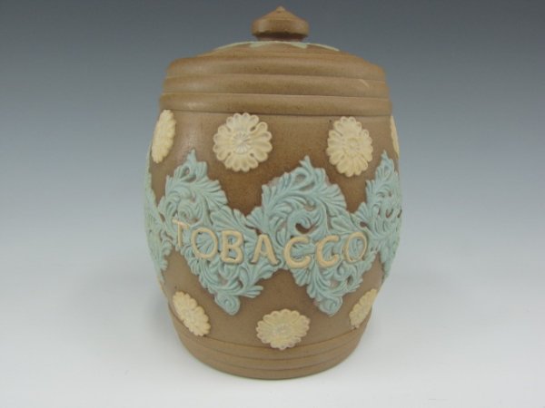 A ROYAL DOULTON LAMBETH SILICON WARE HUMIDOR: Barrel form with embossed polychrome on earthen-brown, floral pattern and "Tobacco," incised Royal Doulton mark, "hd," and silicon marks to bottom. Includes lid. Measures 5.5 inches.