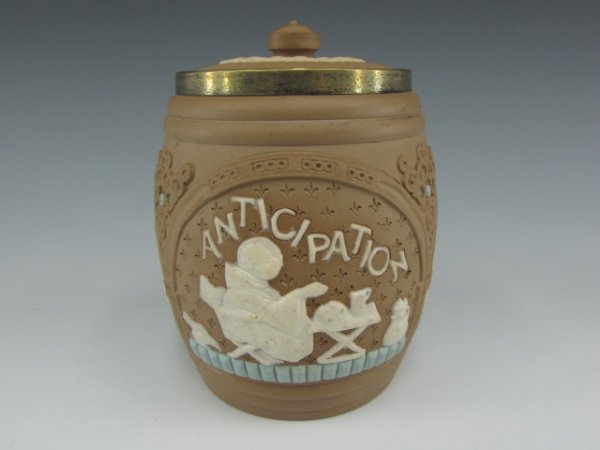 A DOULTON LAMBETH SILICON WARE HUMIDOR: Barrel form with embossed polychrome on earthen-brown, three high relief panels depicting the three stages of a meal, anticipation, realization, gratification. Includes lid. Has metal collar around ri