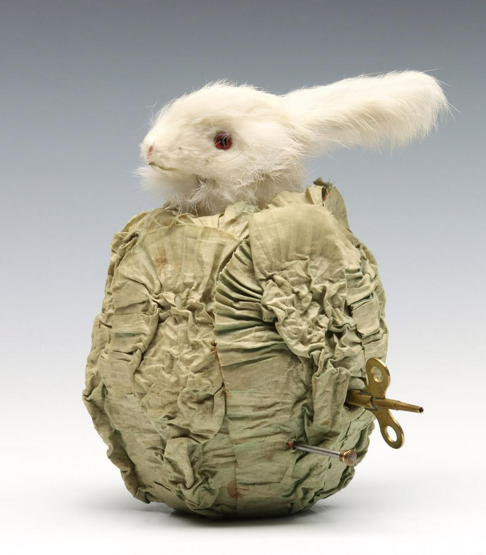 A MUSICAL CLOCKWORK RABBIT IN CABBAGE AUTOMATON C. 1930: The white fur-covered rabbit with brown cheek patch and glass eyes rises from the center of a cabbage turning and titling it's head while the mouth opens and closes to the tune of an internal music bo