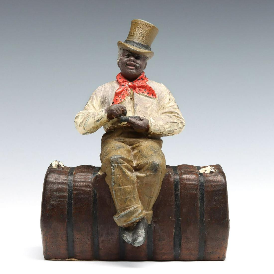 SCARCE EARLY 20TH C. DANDY ON A COTTON BALE DOORSTOP: The painted white metal figure of an African American in top hat with a cigar in his mouth while holding what appears to be a snuff box, he sits on a cast iron bale of cotton, attributed to Judd Compa