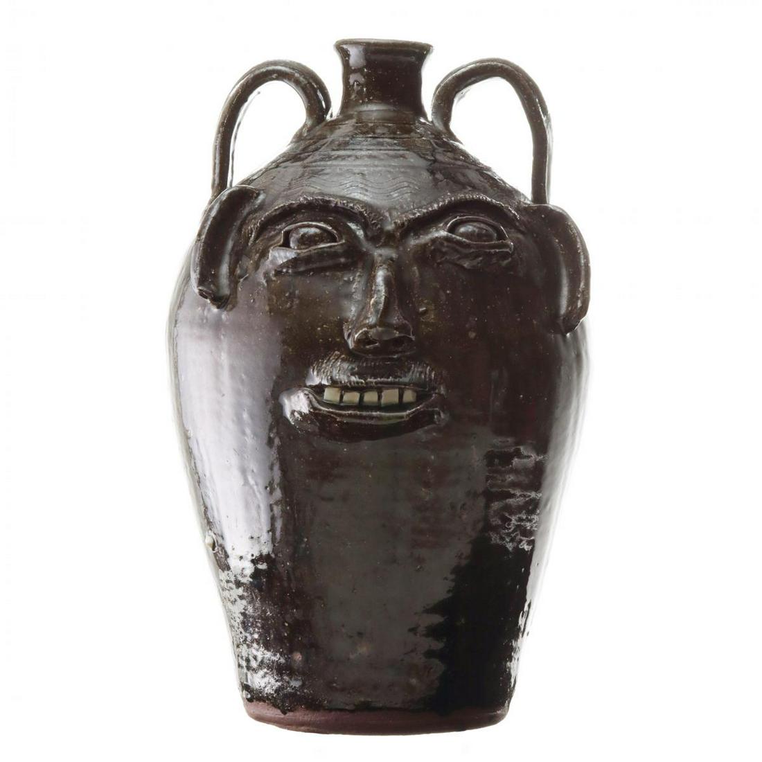 A LARGE STONEWARE FACE JUG SIGNED BB CRAIG VALE NC: Th large two-handled jug with incised concentric rings and 'squiggles' above the applied features and white kaolin ceramic teeth, stamped mark on the underside of the base. Measures 19 x 12 x 14 inche