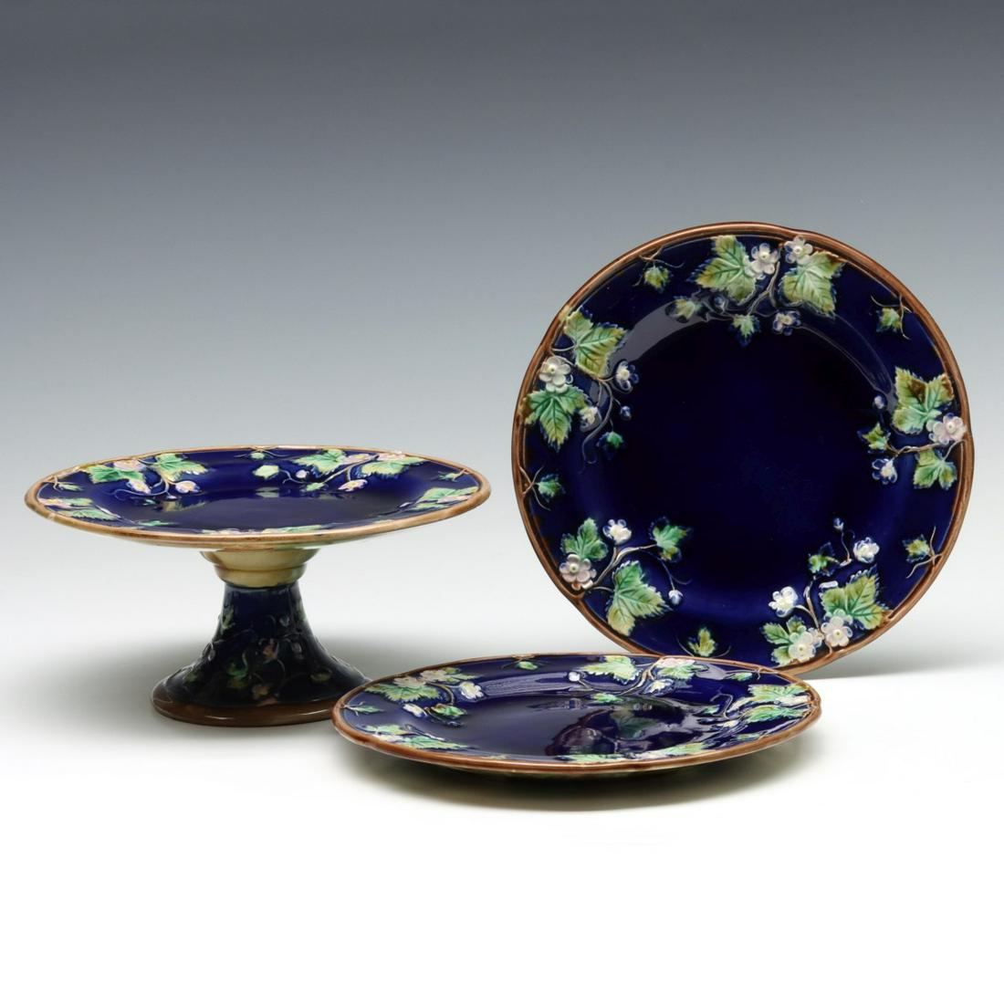 STRAWBERRY BLOSSOM MAJOLICA PLATES AND COMPORT: The cobalt ground plates and comport with strawberry blossoms on cobalt ground, mottled green and brown back sides, unsigned, some have attributed this to George Jones as maker. Plates measure 8.5, co