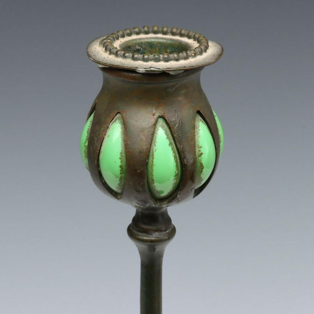 A TIFFANY STUDIOS BRONZE AND BLOWN GLASS CANDLESTICK: The organic form with flattened flowing base and thin rising tendril supporting a candle cup with green glass blown from the interior and slightly outward through each elongated opening in the slightl