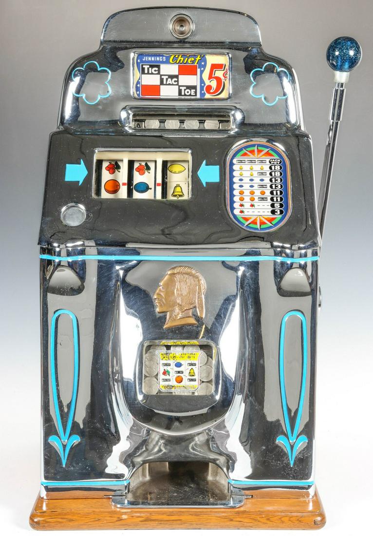 AN O.D. JENNINGS CHIEF 5 CENT TIC TAC TOE SLOT MACHINE: The chrome front three reel model with standard applied brass-colored bust of a Native American, intaglio designs with blue enamel, oak case, circa 1951, complete with keys. Due to the laws regulating