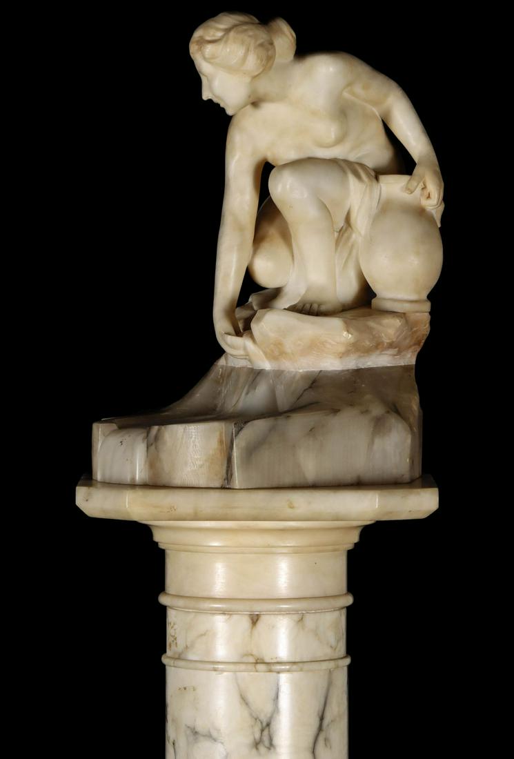 AN ITALIAN NUDE BATHER MARBLE SCULPTURE WITH PEDESTAL: The carved marble figure of a kneeling Classical maiden with robe and urn kneeling on a marble ledge above an alabaster pool, no signature found, circa early 20th century. The sculpture is displayed o