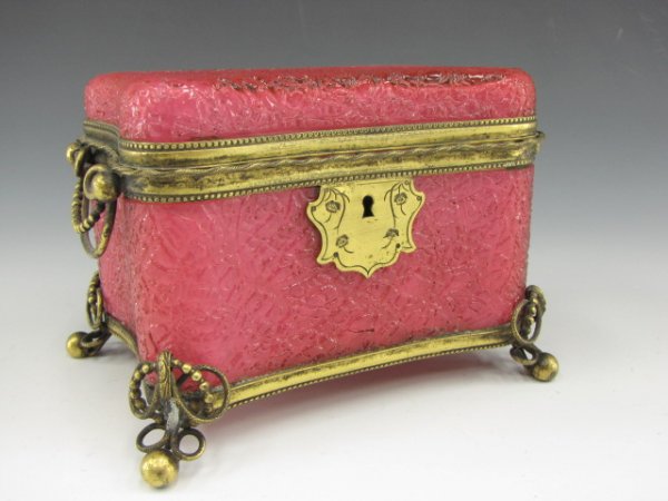 A VICTORIAN CASED CRACKLED CRANBERRY GLASS CASKET: Fine cranberry crackle glass jewelry casket set in an ormolu frame, swivel side handles, four ball feet. The crackled exterior is fused to a white glass interior. Measures 4 x 5 x 4 inches.