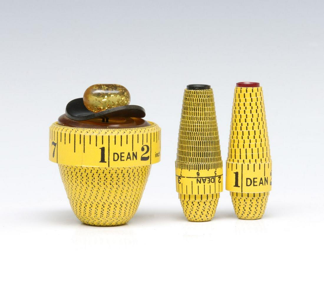 TAPE MEASURE ART NEEDLE AND THIMBLE HOLDERS DATED 1991: Each topped by a vintage button and signed on the base with date of 1991. The functions are presumably needle and thimble holders. Measure 3 inches each. Provenance: The estate of Morton and Estelle S