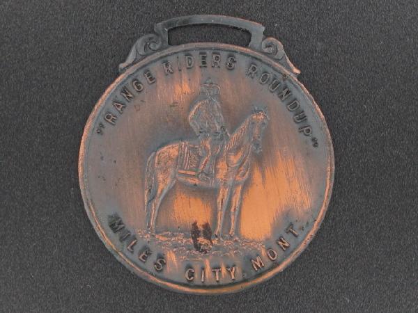 RANGE RIDERS ROUNDUP, MILES CITY, MT ADVERTISING WATCH : Die struck bronze, double-sided with 'Range Riders Roundup, Miles City, Mont.' and mounted rider on obverse, mountain sunrise scene to reverse. Measures 1-3/8 x 1-1/2 inches. Good condition.