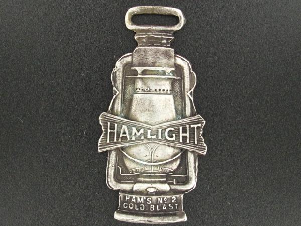 HAMMLIGHT LANTERN COIN SILVER ADVERTISING WATCH FOB: Die struck, double-sided, lantern-shaped fob with Hammlight barn lantern on obverse and 'Ham's No. 2 Cold Blast' below, reverse with stamped 'Coin Silver' above raised lettering, 'The original and onl