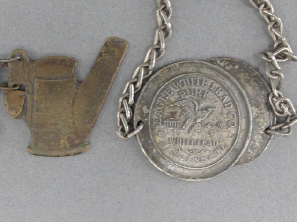 EAGLE WHITE LEAD CO & SIMMONS CLAY BANK FOBS: Die struck iron Eagle White Lead Co fob on chain, fob measures 1.25 x 1-3/8 inches; and a 1-1/8 x 1-1/4 inch brass Simmons Clay Bank Co fob on chain. Both show some wear and toning.