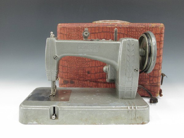 A SEW-RITE M-7 ELECTRIC TOY SEWING MACHINE: Grey finished metal machine with cord and plug, spec plate affixed to motor; simulated alligator skin covered paper case, measures 8.5 x 12 x 7.5 inches overall.