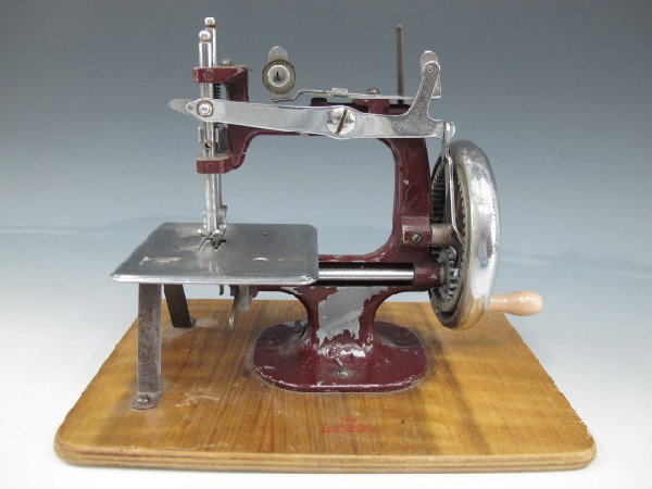 THE ESSEX TOY SEWING MACHINE: Burgundy paint on metal, hand cranked, measures 7 x 9 x 6.75 inches.