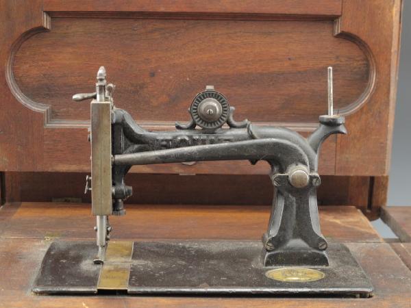 A HOWE STOCKWELL BROTHERS SEWING MACHINE, CIRCA 1867: Fantastic Howe machine in hinged folding wooden case, on wooden base. Inset Howe medallion, serial numbered 154983, stamped with 1867 patent date, same year inventor Elias Howe died. Machine measures