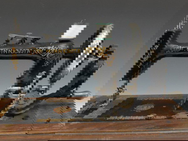 A MINNESOTA HAND CRACK SEWING MACHINE, CIRCA 1908: Black with gold and red decorations, 'Minnesota' across head, and logo on plate. Stamped needle plate with presumed serial number, D1683221, and thread board. J.W. Slaten's 'Antique American Sewing Ma