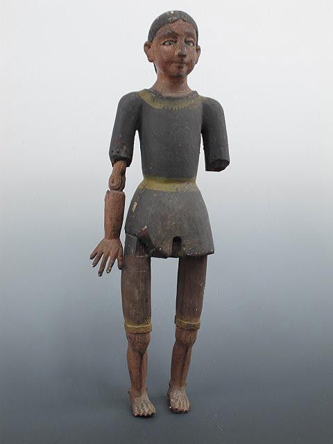 A CARVED WOOD SANTOS FIGURE WITH GLASS EYES: Carved wood figure of a man, missing half of one arm, other arm hinged; glass eyes, stands 15.5 inches.