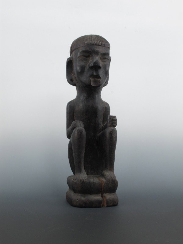 OCEANIA CARVED WOOD FIGURE: Single piece carved wood seated figure, holds a cup in its left hand. Measures 21 x 6 x 6 inches.