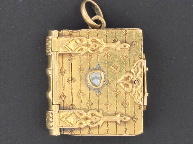 A VICTORIAN GOLD BOOK FORM LOCKET WITH DIAMOND: Hinged book with front centered by a rose cut diamond, both front and side open to reveal interior, measures 1" x .75", weighs 13 grams.