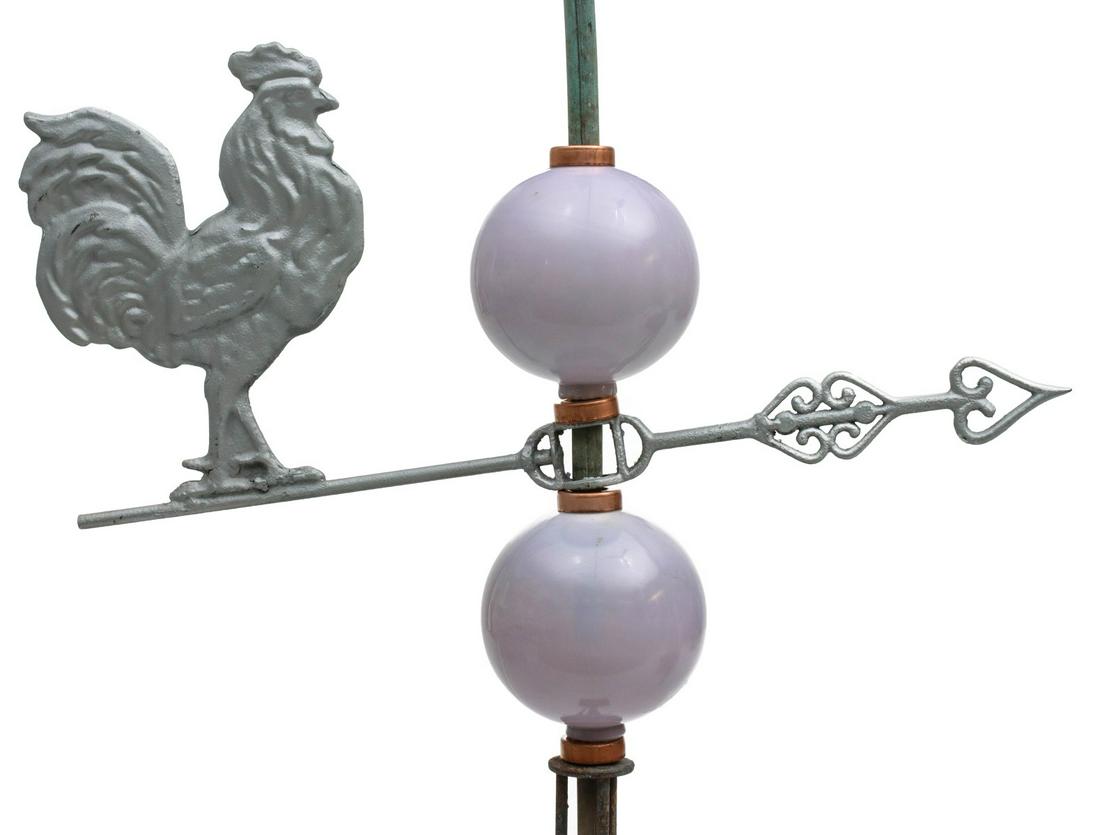 A LIGHTNING ROD WEATHER VANE WITH ROOSTER AND GLOBES: The full-bodied iron rooster mounted on a fancy iron directional, silver paint, two lavender colored milk glass globes, all mounted on a copper spindle with bayonet top and iron brace. Measures 62.5 x