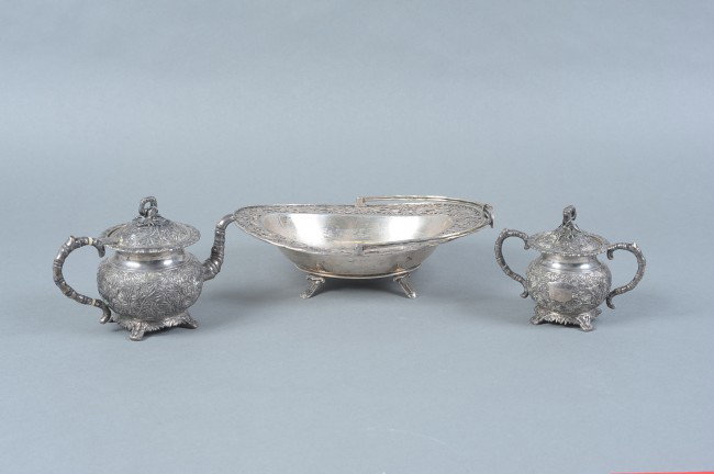 CUM WO AND ZEE WO CHINESE EXPORT SILVER: A silver footed basket with openwork bamboo design rim and a hinged bamboo motif arching handle, two hallmarks for Zee Wo, Shang Hai, circa 1900. Measures 5" x 4" across the handle and the spout. Plus