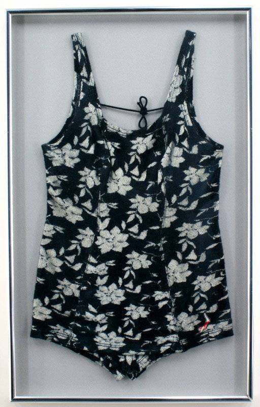TWO LADIES JANTZEN VINTAGE WOOL SWIMSUITS: One black floral design Jantzen swimsuit with the Jantzen logo patch on the lower left leg. Suit measures 28.5 x 16.5 inches in a 32 x 20 inch frame. One navy blue Jantzen swimsuit with the Jantzen lo