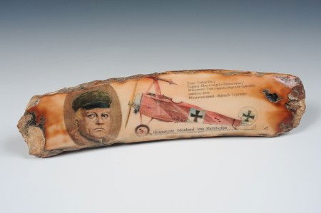 THE RED BARON FOSSILIZED WALRUS TOOTH: A fossilized walrus tooth with scrimmed image of Rittmeister Manfred von Richthofen, 'The Red Baron,' along with his Fokker tri-plane, signed L in lower right corner. Measures 8 inches in length.