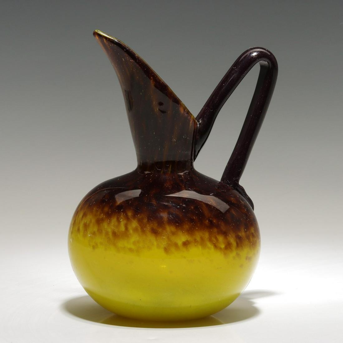 A FRENCH ART GLASS JUG SIGNED SCHNEIDER CIRCA 1925: Charles Schneider (1881-1952) The bulbous Bijou glass jug with elongated spout is shaded by internal powder inclusions from aubergine to yellow accented by an applied aubergine strap handle with ribbo