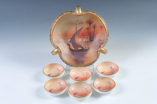 A NIPPON SCENIC PAINTED NUT SET: A tricorn nut bowl with looping handles and an interior scene of a Middle Eastern coast, measures 8.5" x 3.75", green wreath mark. Plus six matching footed nut cups that measure 1" x 3".