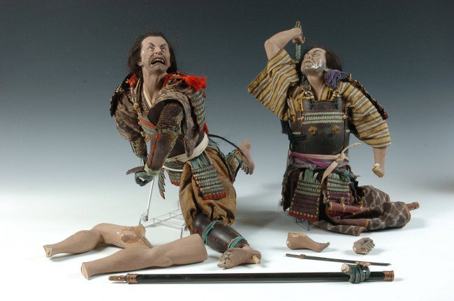 A PAIR OF JAPANESE SAMURAI WARRIOR DOLLS: Two wooden samurai dolls poised with swords and staff. Both very worn and need multiple repairs and mends. Includes two swords, one like a wakizashi, other like a katana. Also a staff. Armor and costu