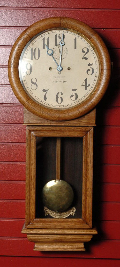 A NEW HAVEN 'SATURN' WALL CLOCK IN OAK CASE: Thirty day, spring powered, time only, in oak, gold painted iron beat plate, old paper dial replacement(?), meaures 35 x 15.5 x 6.5 inches overall. Good running condition. Running condition is not gua