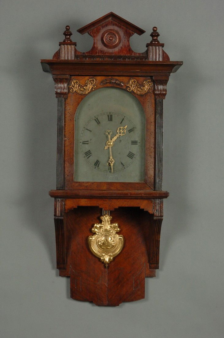 A GERMAN WALL CLOCK WITH OPEN WAG: With fancy Art Nouveau pendulum, nice veneers, metal dial, added crest, measures 33 x 15.5 x 7.5 inches overall.