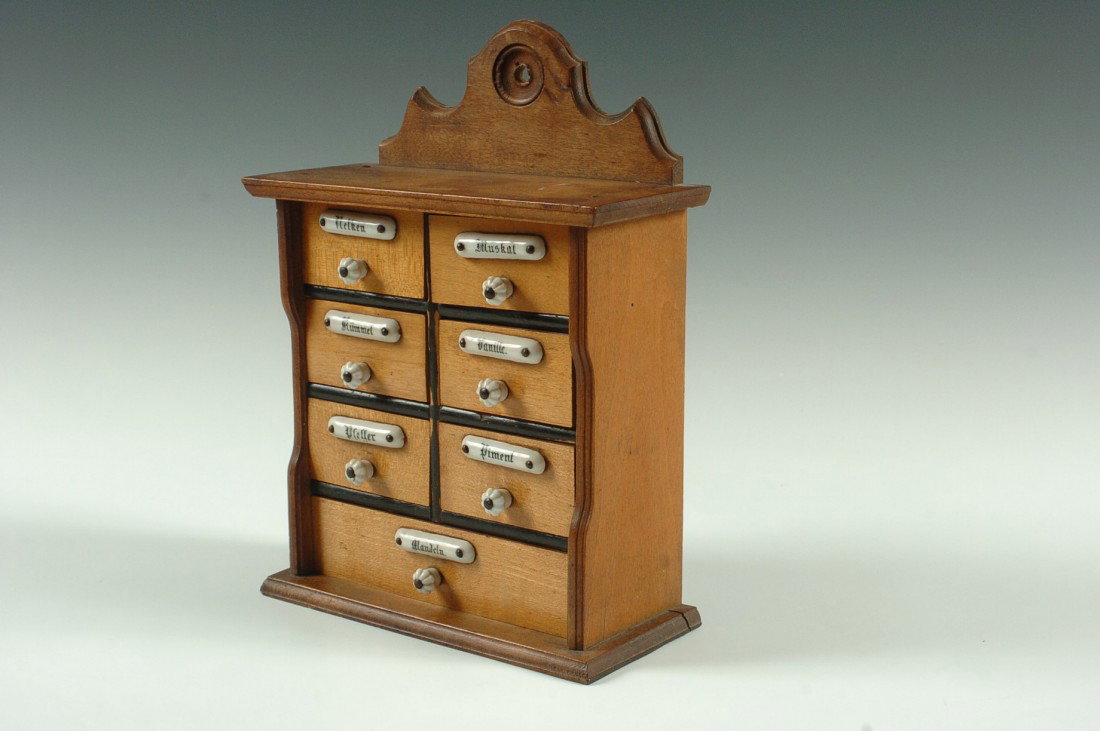 SMALL ANTIQUE SPICE CABINET WITH ENAMEL TAGS: Seven drawers, each with a porcelain knob and long oval half-round tag naming various spices - Nutmeg, Almonds, Pepper, Allspice, Vanilla and Cumin - all in German, circa 1875. Measures 10 x 7.5 x 3.5