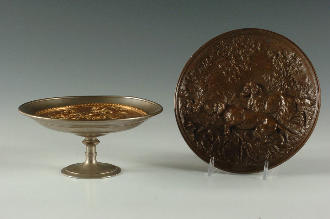 TWO VICTORIAN BRONZE PLAQUES: One with a classical scene, set in a tazza, 3 x 6.75 inches. Other with two dogs, three footed base, 7.25 inch diameter.