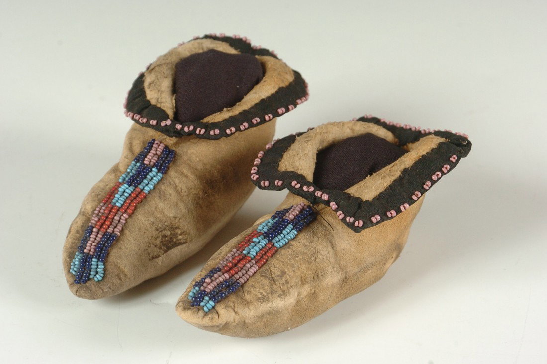 PRAIRIE BEADED CHILD'S MOCCASINS CIRCA 1870s: Pair of Prairie (possibly Kickapoo) child's moccasins partially beaded in dark and light blue, red, and pink geometric designs; the cuffs are decorated with black trade cloth interspersed with pink be