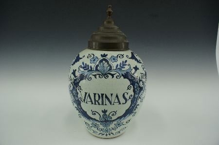 A DELFT VARINAS TOBACCO JAR, SIGNED DE KLAUW: From the De Porceleyne Klauw, established at Delft, Holland in 1662; with the 'claw' mark underneath. 'Varinas' and floral decorations are the front design. Measures 10.75 x 8.5 inches.