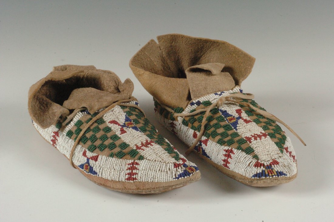 A PAIR OF ARAPAHO BEADWORK MOCCASINS C. 1910: Sinew sewn beaded moccasins with white-heart red, navy blue, greasy yellow, green and white, parfleche bottoms, native worn, approximately 8 inches long. Purchased from Trade Winds Gallery in 1978.