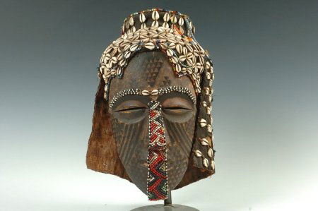 BALUBE LUEUMBASHI CHIEF'S MASK, ZAIRE: Carved wood mask with painted black geometric designs and beaded accents on the eyebrows and down the nose and mouth. Bead and cowry shell hair with a fabric and canvas hat and back. Used only at the