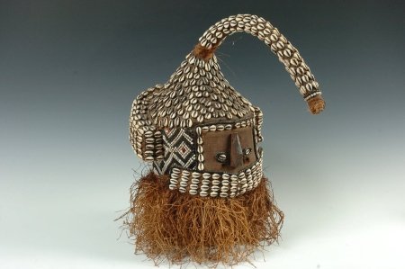 BAKUBA HEADRESS, CONGO (ZAIRE): Canvas on a wooden frame, human face with a wooden nose and ears, eyes of cowry shells and beads, horn and head is covered in cowry shells with beadwork around the sides and a raffia fringe around the