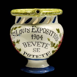 A 1904 ST. LOUIS WORLD'S FAIR SOUVENIR PUZZLE MUG: The Italian faience puzzle mug states 'St. Louis Exposition 1904 Bevete Se Potete (Drink If You Can),' signed with a maker's mark on the base. Measures 5 x 6.25 x 4 inches. Without proof of