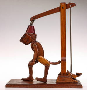 A 1930s FOLK ART TOY ATTRIBUTED TO A KANSAS INMATE: The animated figure of a performing monkey with tack eye and a red fez is carved from walnut and articulated on simple brass fittings. The red fez has a nice original alligatored finish. Similar