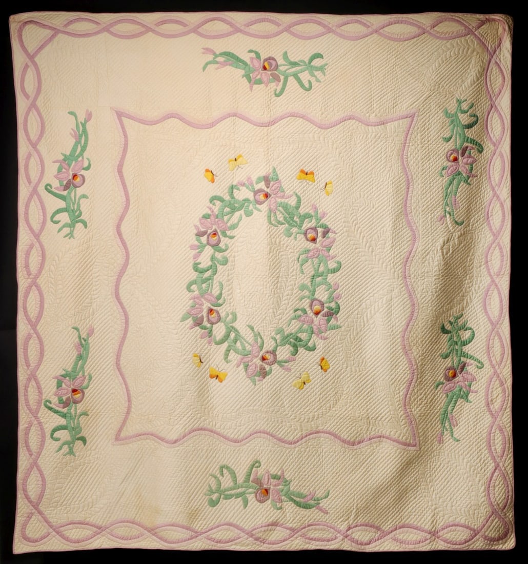 A VINTAGE WREATH AND BUTTERFLY APPLIQUE QUILT: The central appliqued floral wreath with butterflies and ribbons is surrounded by pastel motifs of floral sprays and frames of intertwined ribboning, pink backing and binding. The whitework areas are 