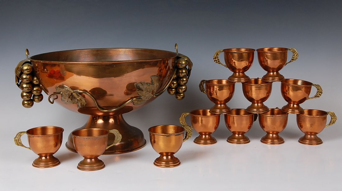 COPPER PUNCH BOWL AND TWELVE CUPS: Fine pedestal copper punch bowl with brass grape bunch side handles and applied vine work. Measures 9 x 14 inches; cups measure 3 x 3.25 inches. Unmarked.