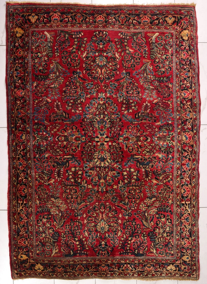 A 1930s PERSIAN SAROUK HAND KNOTTED AREA CARPET: The typical wine red field is arranged with tightly packed floral sprays surrounding flowering trees at each end and central design of similar design end-to-end. The dark blue border encloses a flower