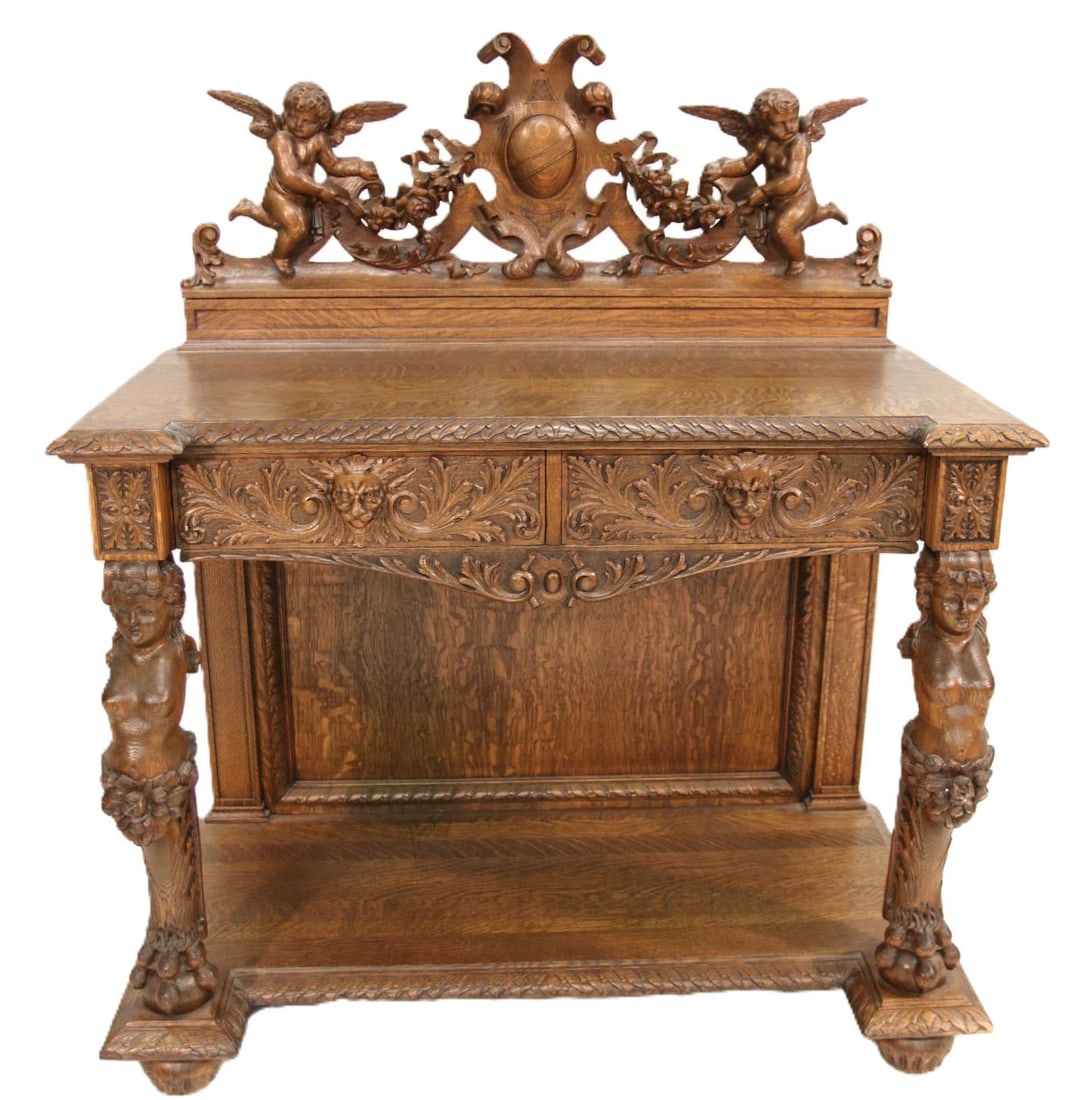 AN R. J. HORNER CARVED OAK SERVER WITH LARGE CHERUBS: The handsomely carved server is topped by an openwork crest of full-bodied cherubs in flight draping a garland of flowers each side of the central cartouche shield over a flat top having outset front 