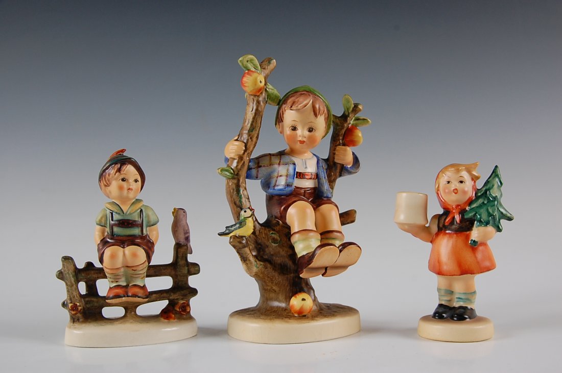 THREE HUMMEL FIGURINES, APPLE TREE BOY, WAYSIDE HARMONY: Includes Apple Tree Boy, 142/1, measures 5.75 x 4 inches; Wayside Harmony, 111, measures 3.75 x 2.75 inches; and girl with fir tree candleholder, measures 2.5 x 2.25 inches.