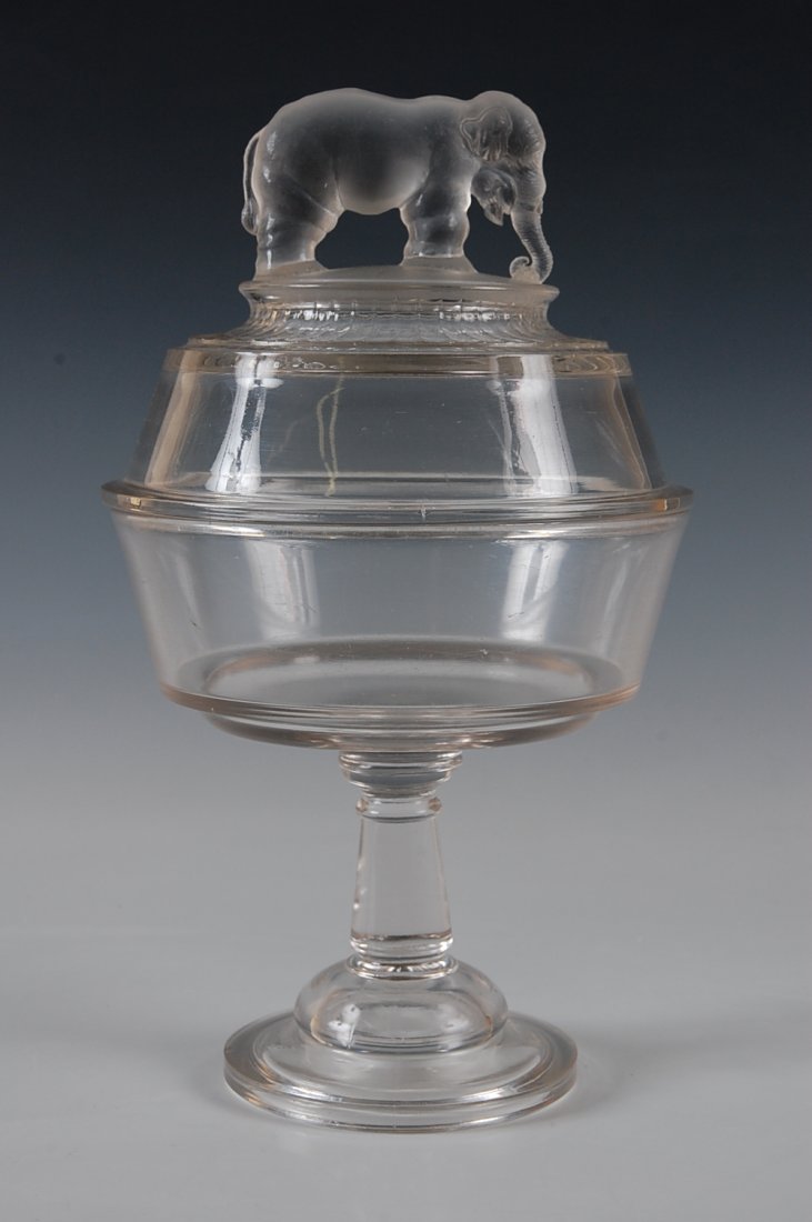 JUMBO EAPG HIGH STANDARD COVERED COMPOTE: Two piece base with wafer construction, frosted figure of Jumbo standing on frosted ground, his truck curled trunk around a clump of hay. The measurements are 12 inches high by 7 inches diameter..