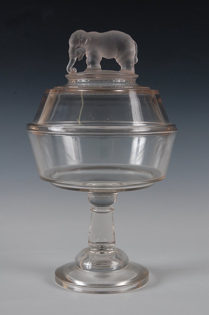 JUMBO EAPG HIGH STANDARD COVERED COMPOTE 8 INCHES : Two-piece base with wafer construction, frosted figure of Jumbo standing on frosted ground, his trunk curled trunk around a clump of hay. The measurements are 13 inches high and 8 inches diameter.