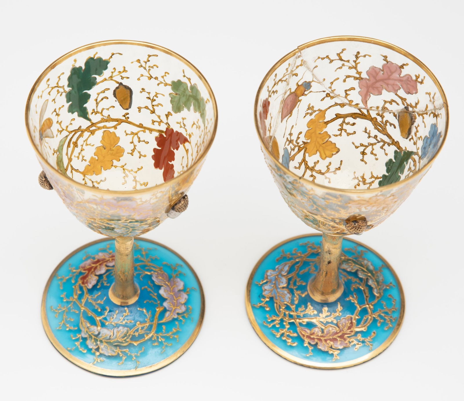 AN UNUSUAL WINE GOBLET WITH APPLIED ACORNS SIGNED MOSER: The colorless crystal bowl with relief enamels of oak boughs is further embellished with three art glass acorn applications, and raised on a gilded stem emanating from a brilliant blue foot with match