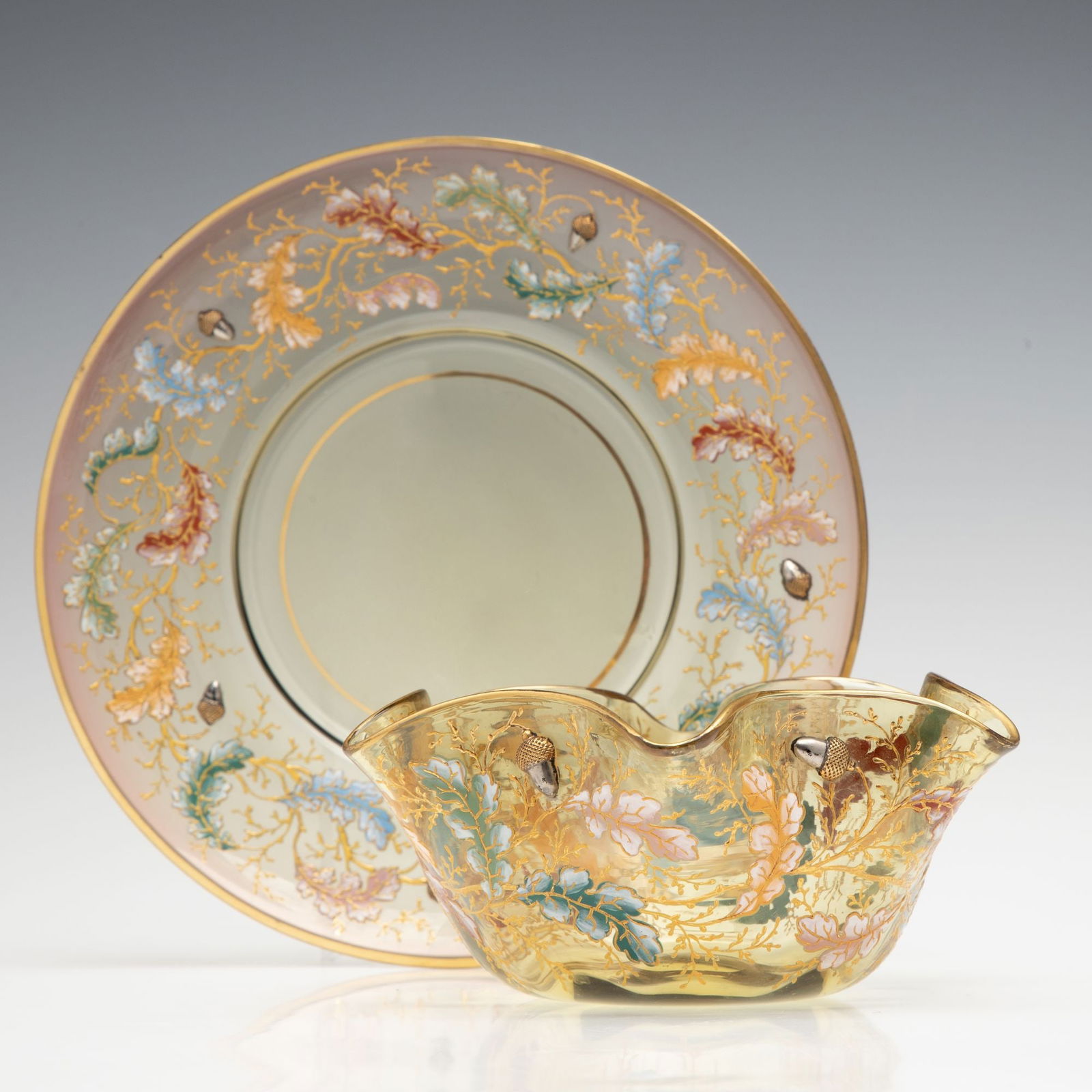 ENAMELED MOSER FINGER BOWL AND UNDERPLATE WITH ACORNS: Ludwig Moser Late 19th Century The topaz colored glass is blown with a rose tint near the edge and decorated in polychrome relief enamel oak boughs embellished with applied art glass acorns having a g