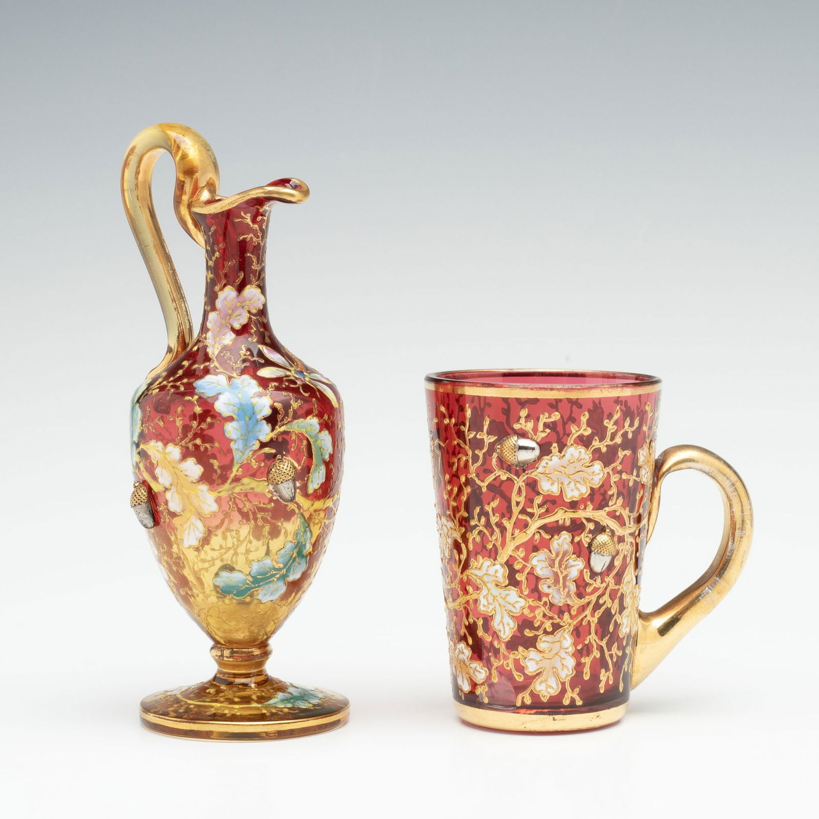 MOSER AMBERINA AND CRANBERRY GLASS MINIATURES W/ACORNS: Ludwig Moser. Late 19th Century. Each example is embellished with gilt and enamel decoration of oak boughs and insects interspersed with applied art glass acorns. Measures 2.75 x 2.75 x 1.75 and 4.75