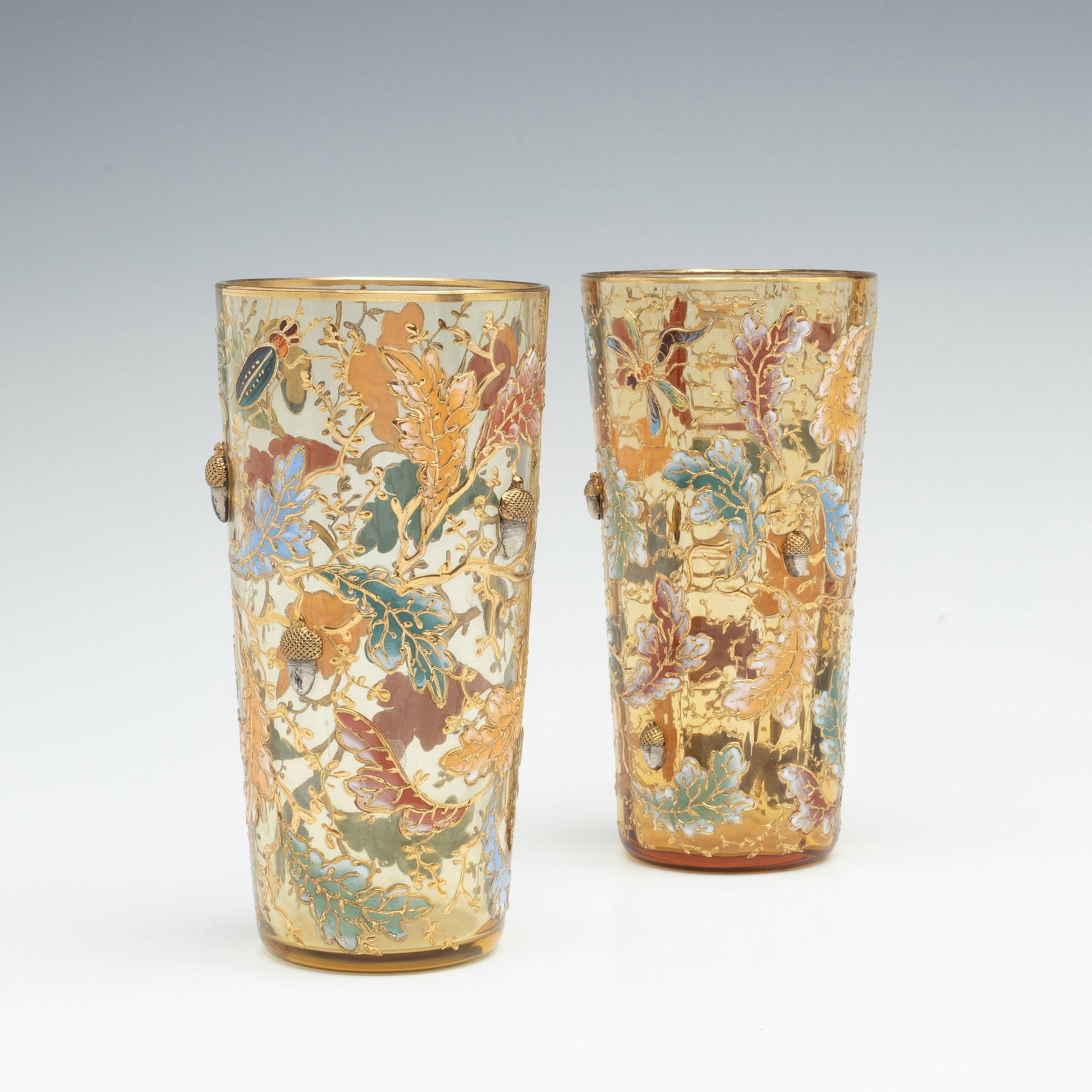 MOSER GILT AND ENAMEL BEAKERS WITH INSECTS AND ACORNS: Ludwig Moser Late 19th Century The light topaz art glass pair are each decorated with colorful oak boughs and a large insect in relief enamel, along with five large art glass acorns having gilt crossh